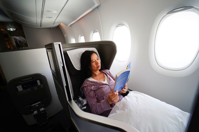 Женщина отдыхает с книгой на борту самолета первого класса