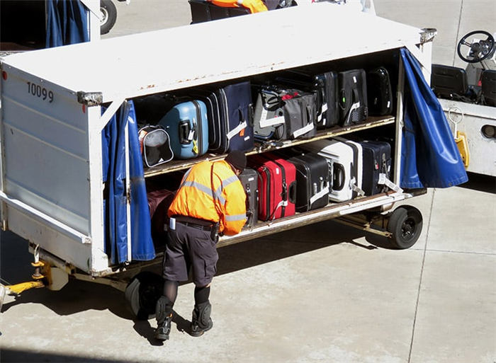 работник багажного отделения выгружает зарегистрированный багаж из грузовика в аэропорту