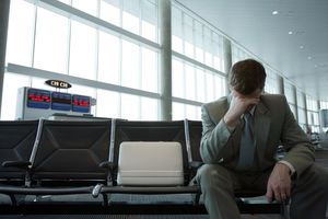 Бизнесмен сидит в зале ожидания аэропорта, держась за голову