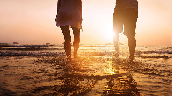 Пара гуляет в воде на закате на пляже.