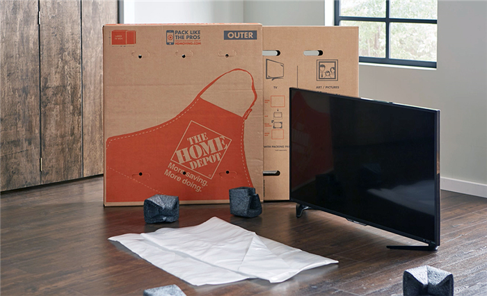 Коробка для переезда The Home Depot рядом с телевизором с плоским экраном.