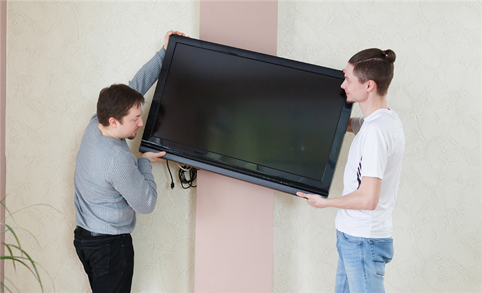 Два человека крепят телевизор с плоским экраном к стене.