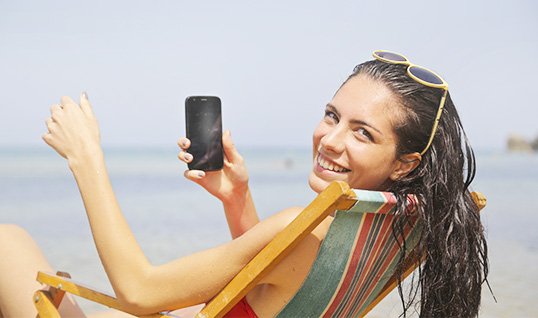 Женщина сидит на пляже и держит в руках мобильный телефон