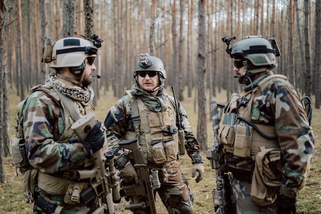 Группа бородатых солдат средних лет в военной форме и тактических жилетах обсуждает план действий
