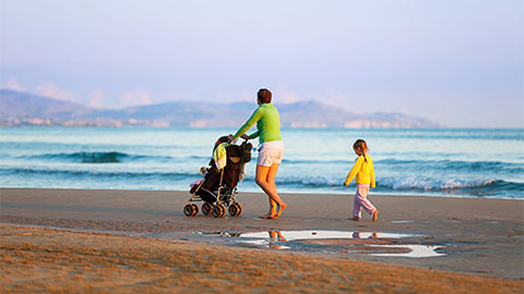 Женщина с ребенком на пляже с детской коляской.