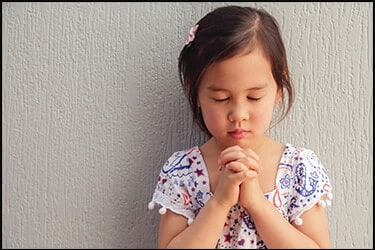 Маленькая азиатская девочка молится с закрытыми глазами